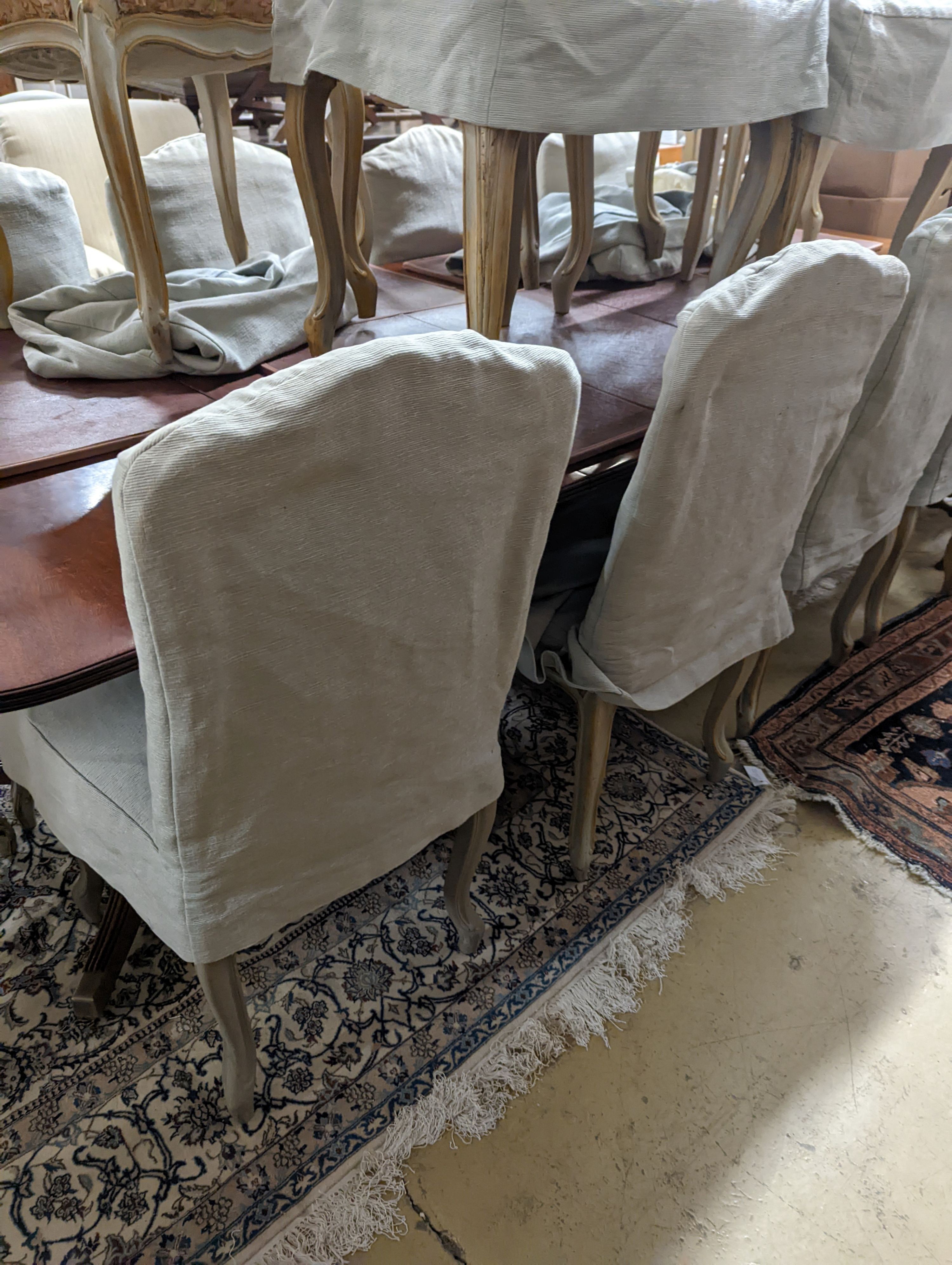 A set of fourteen French Louis XV style painted upholstered dining chairs with loose covers